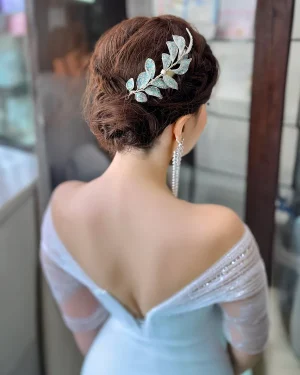 Tocado de novia con hojas en resina Melina Tocado de novia con hojas en resina diseñado para aportar un acabado ligero y delicado al peinado. El modelo Melina destaca por sus pequeñas hojas con acabado brillante, que capturan la luz de forma suave, generando un efecto sutil que realza el look sin sobrecargar. Su tamaño compacto lo convierte en una opción ideal para quienes buscan un detalle discreto pero con personalidad. Este tocado de novia con hojas en resina se integra con facilidad en distintos estilos de peinado: Recogidos elegantes Moños suaves Semirecogidos naturales Puede colocarse en diferentes zonas del cabello, logrando un acabado limpio que acompaña el peinado con armonía. Su estructura ligera permite llevarlo cómodamente durante toda la celebración, manteniendo firmeza y un ajuste seguro. Una opción ideal para novias que buscan un accesorio sutil, fácil de combinar y con un toque especial. 📏 Detalles Material: Resina Diseño: Hojas brillantes Estilo: Ligero / Delicado / Natural Uso: Novia Medidas: 12 cm aprox. Puede existir una pequeña variación en el tamaño.