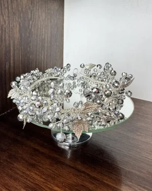 Corona de novia plateada con perlas y cristales Pasión Corona de novia plateada con perlas y cristales diseñada para aportar un acabado llamativo y lleno de carácter al peinado. El modelo Pasión combina abundantes perlas plateadas con cristales brillantes, creando un efecto visual intenso que destaca desde cualquier ángulo. Su diseño resalta la luz de forma elegante, ideal para novias que desean un look con presencia y personalidad. Esta corona de novia plateada con perlas y cristales es perfecta para peinados donde se busca un detalle protagonista que complemente el conjunto: Recogidos estructurados Moños altos o bajos Peinados pulidos Su forma permite integrarla de manera firme, aportando un acabado definido que enmarca el peinado con fuerza y estilo. A pesar de su impacto visual, su estructura ligera permite un uso cómodo durante toda la celebración, manteniendo estabilidad y ajuste seguro. Una opción ideal para novias que buscan un accesorio con carácter, brillo y una estética sofisticada. 📏 Detalles Material: Perlas plateadas y cristales Color: Plateado Estilo: Glamour / Impactante / Sofisticado Uso: Novia Medidas: 39 cm aprox. Puede existir una pequeña variación en el tamaño.