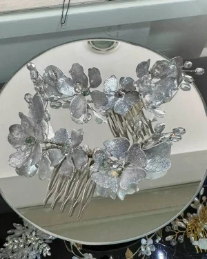 Tocado de novia en resina con cristales | Modelo Fernanda Este tocado de novia en resina está compuesto por dos delicados peines con flores plateadas y cristales brillantes, diseñados para aportar un toque elegante y luminoso al peinado nupcial. Su diseño armonioso permite realzar el look sin sobrecargarlo, manteniendo un estilo sofisticado y femenino. Los detalles en cristal generan un brillo sutil que ilumina el peinado, convirtiendo este accesorio en una opción ideal para novias que buscan equilibrio entre elegancia y delicadeza. ✨ Versatilidad para distintos peinados Gracias a su diseño en dos piezas, este tocado permite adaptarse a diferentes estilos: A ambos lados del peinado para un efecto equilibrado En la parte trasera para destacar recogidos Integrado en trenzas o semirecogidos para un look romántico Su estructura liviana asegura comodidad durante toda la celebración. 💫 Diseño elegante y detalles que destacan La combinación de flores plateadas con cristales crea una estética limpia y sofisticada, ideal para complementar tanto vestidos clásicos como modernos. Este tocado de novia con cristales aporta un acabado delicado que realza la belleza natural. 🖐️ Accesorio cuidadosamente elaborado Cada pieza es trabajada con dedicación, logrando un acabado fino y detallado. Al tratarse de un producto con elaboración cuidada, pueden existir pequeñas variaciones que hacen cada tocado único. 📌 Detalles del producto Material: Resina, cristales y metal Color: Plateado Estilo: Elegante Uso: Novia Medidas: Peine grande: 14 cm aprox. Peine pequeño: 9 cm aprox. Puede existir una leve variación en el tamaño.